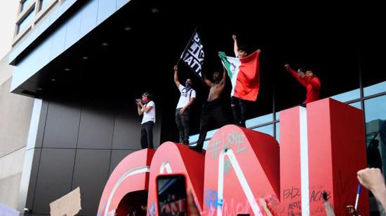 有示威者爬上CNN标志,并挥舞印有“黑人的命也是命”的旗帜。图源:CNN